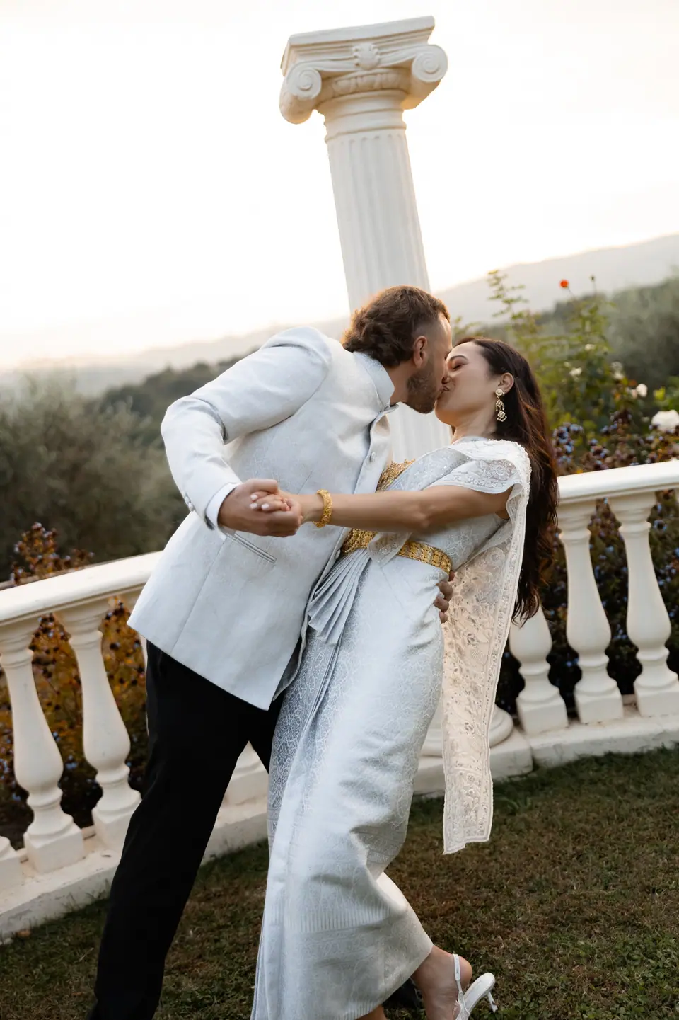 Rory dipping Sivitha into a kiss beside a stone balustrade and columns