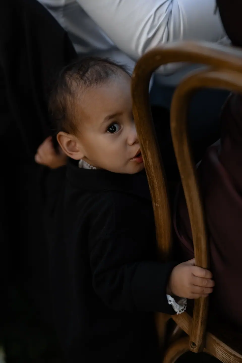 A small boy in a suit peeking out from behind a bentwood chair