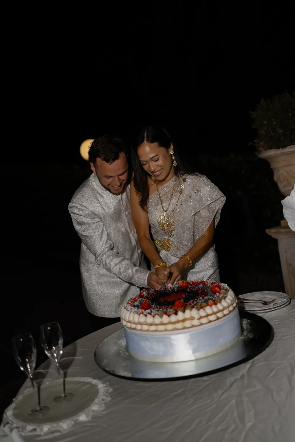 Sivitha and Rory cutting a berry-topped cake at night