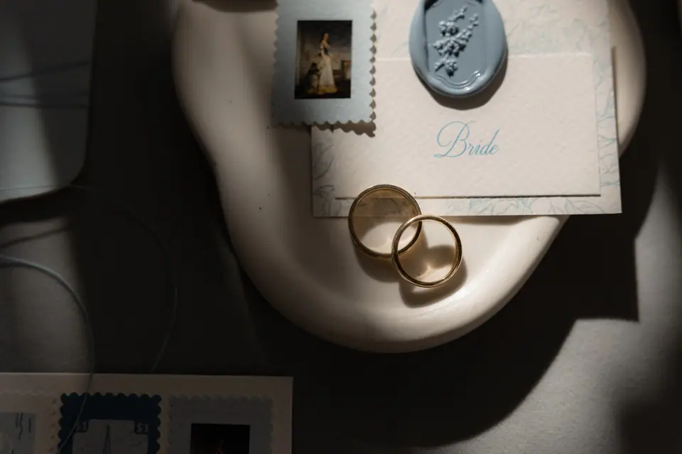 Two gold rings on a place card marked Bride, with a blue wax seal and a small stamp