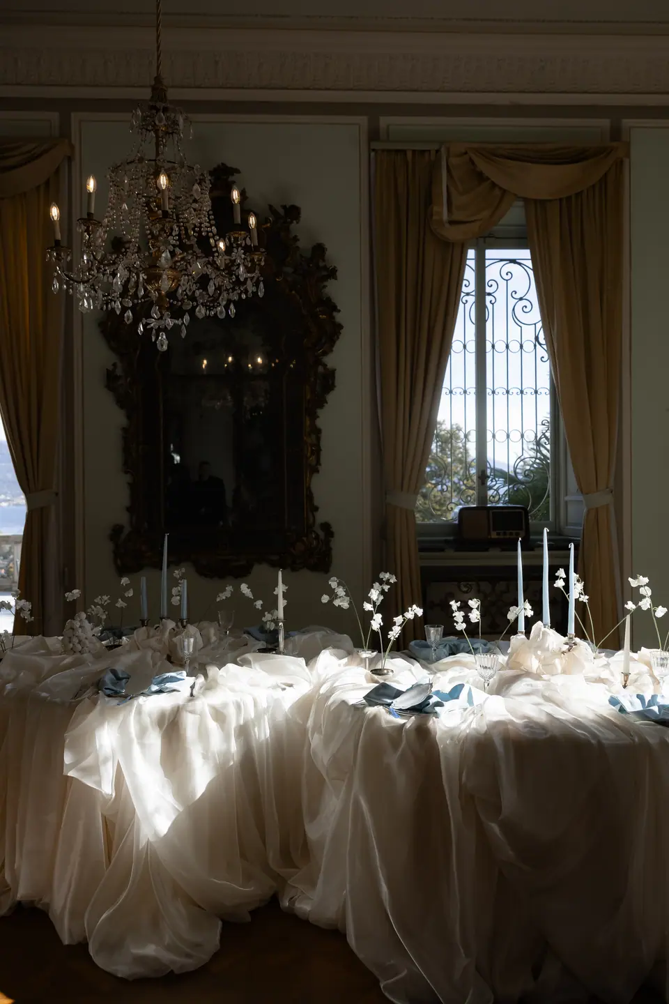 Banquet table draped in cream fabric beneath a chandelier and gilded mirror