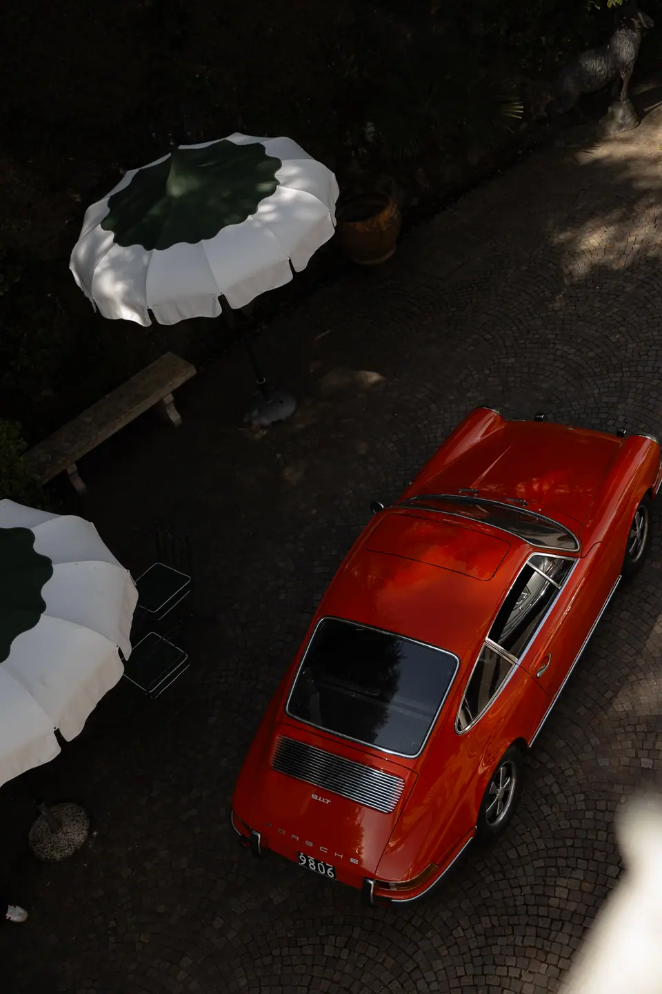 A red vintage Porsche seen from above beside white and green parasols