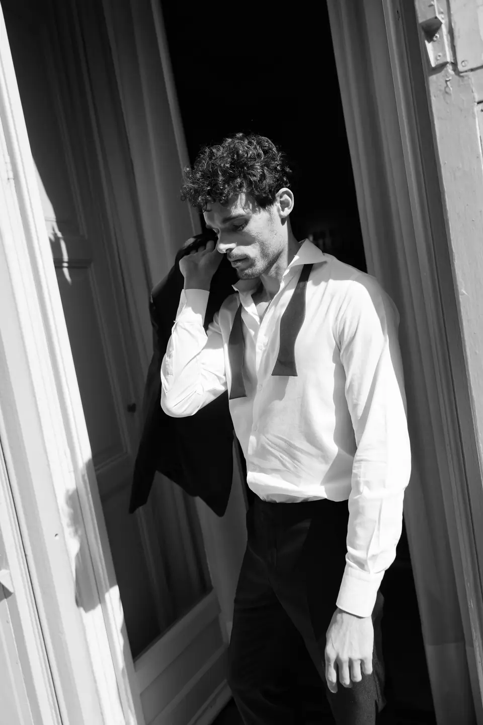 Antoine in black and white by an open door, his jacket slung over his shoulder