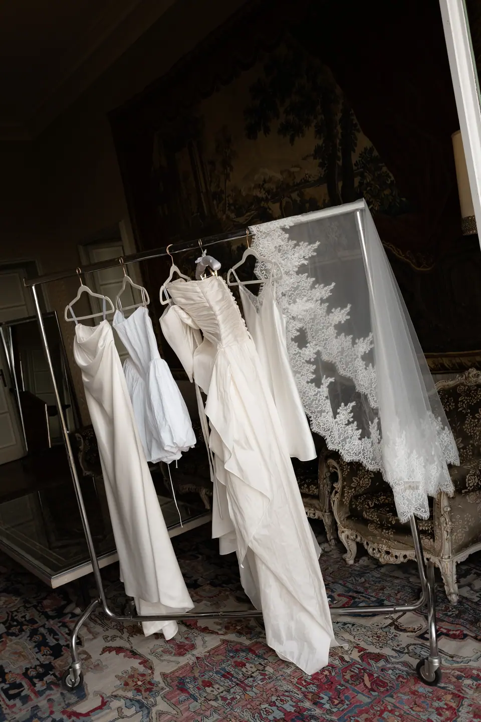 Wedding dress and short dresses on a rail beside a long lace veil