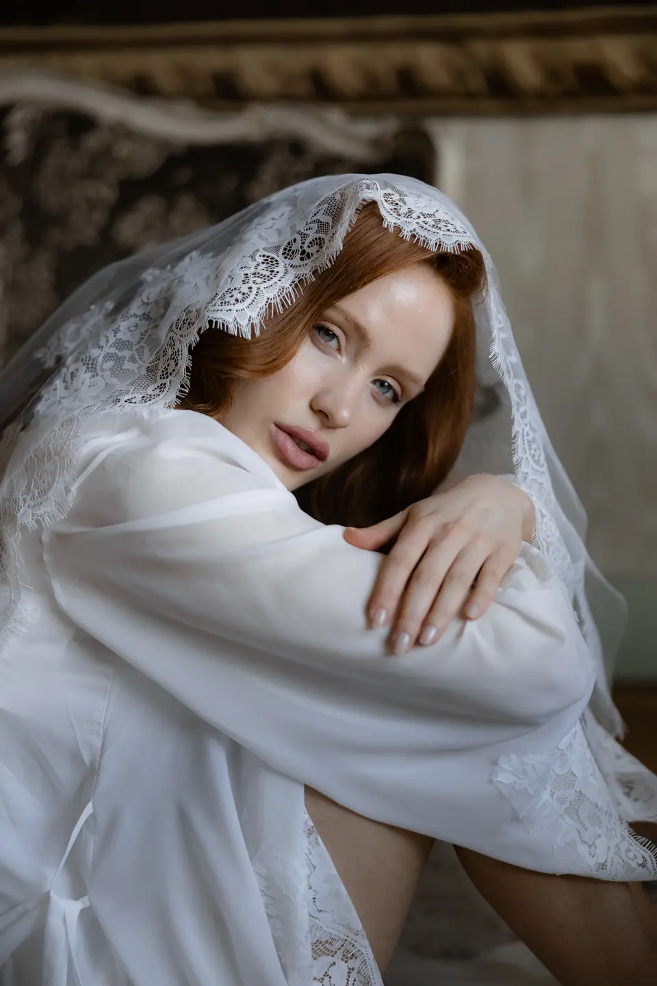 Roberta in a white robe and lace veil, her arms folded over her knees