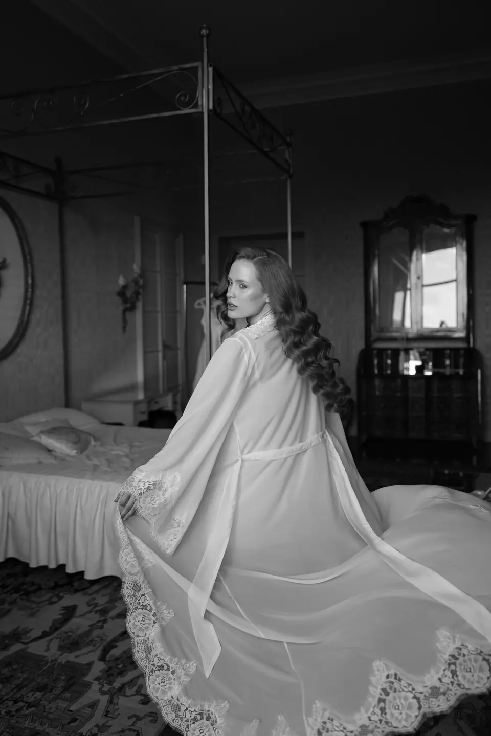 Roberta in black and white in a sheer lace-trimmed robe on a four-poster bed