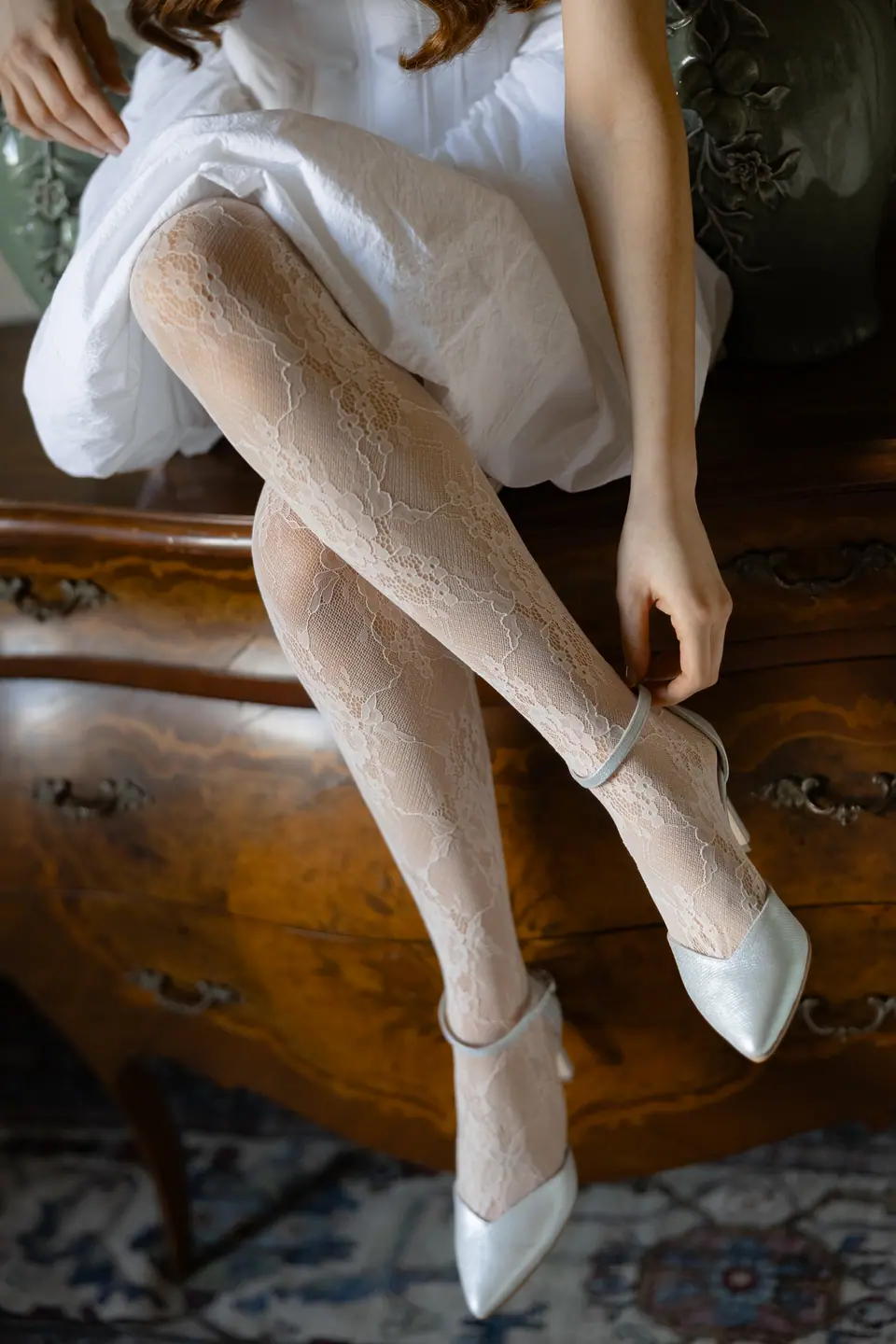 Roberta fastening an ankle strap on a white lace stocking and satin shoe