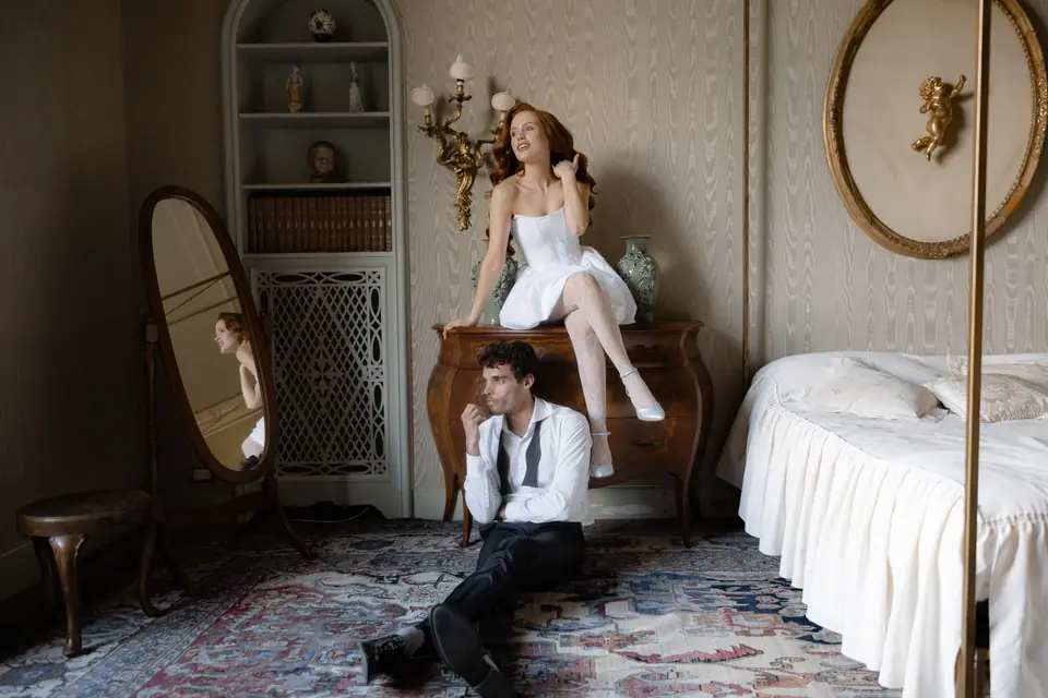 Roberta perched on a dresser while Antoine sits on the floor in a bedroom of the villa