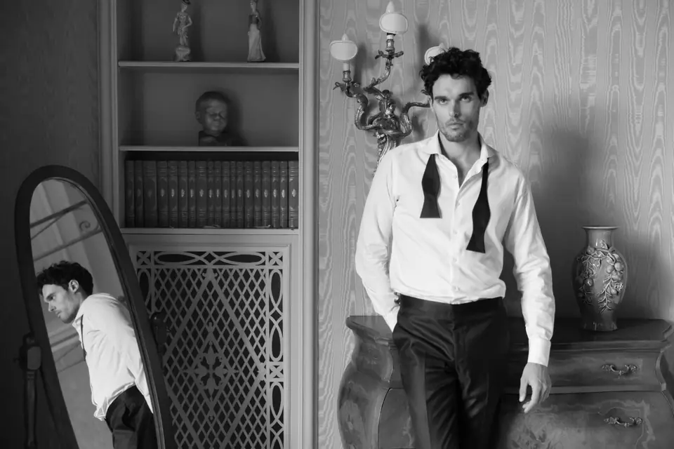 Antoine in black and white leaning on a dresser beside a mirror