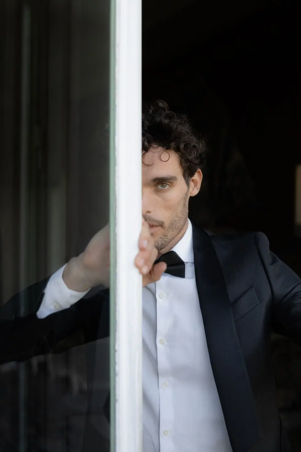 Antoine half hidden behind a window frame in a dinner jacket and bow tie