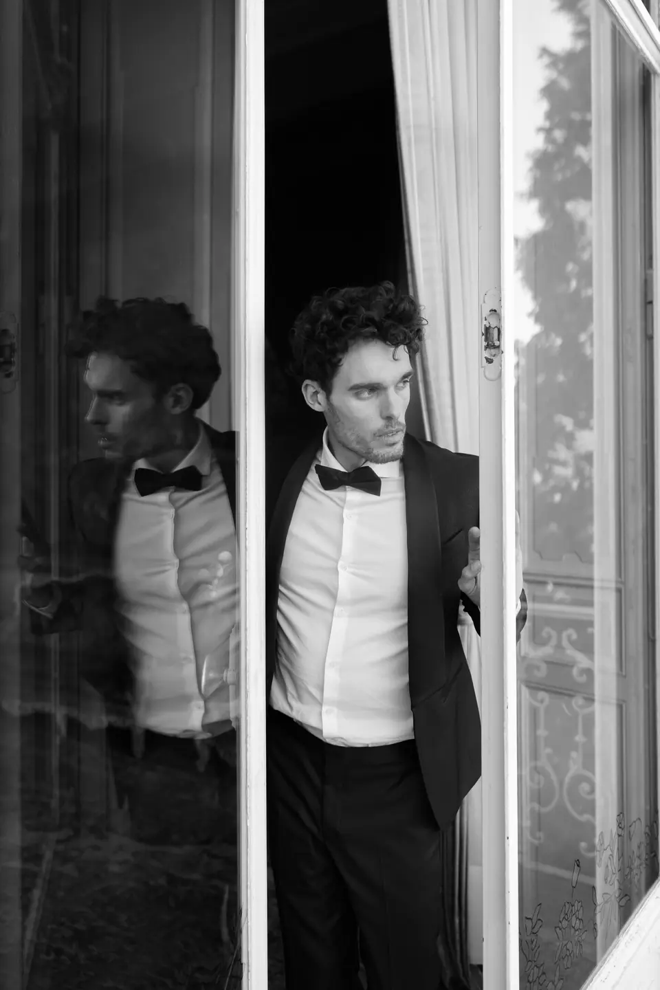 Antoine in a bow tie in front of an open window, his reflection beside him, in black and white