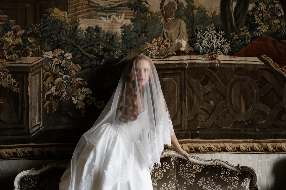 Roberta veiled before a tapestry, seated on an antique sofa