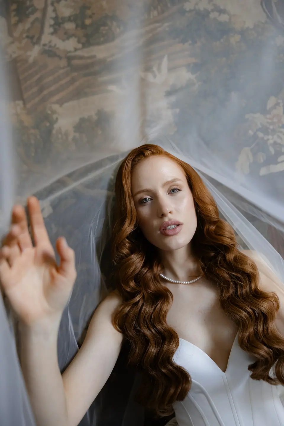 Roberta in a pearl necklace and veil, her hand raised against sheer fabric