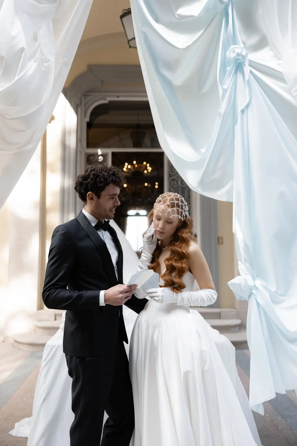 Antoine reading a letter to Roberta between pale blue drapes