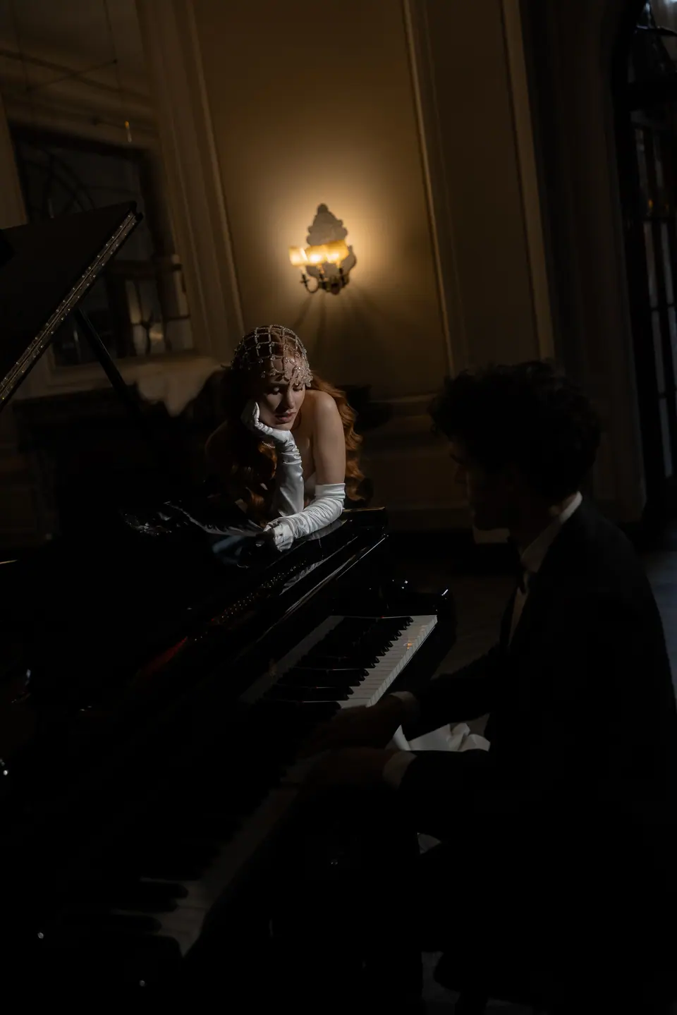 Roberta leaning on a grand piano while Antoine plays, in the dark
