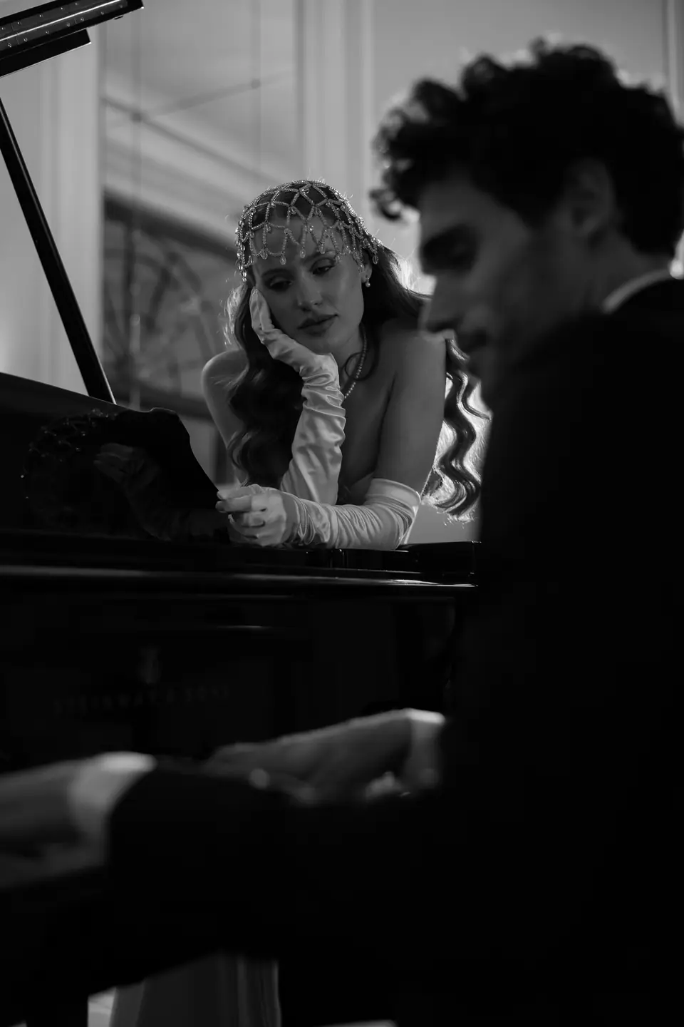 Roberta resting her cheek on her hand as Antoine plays the piano, in black and white