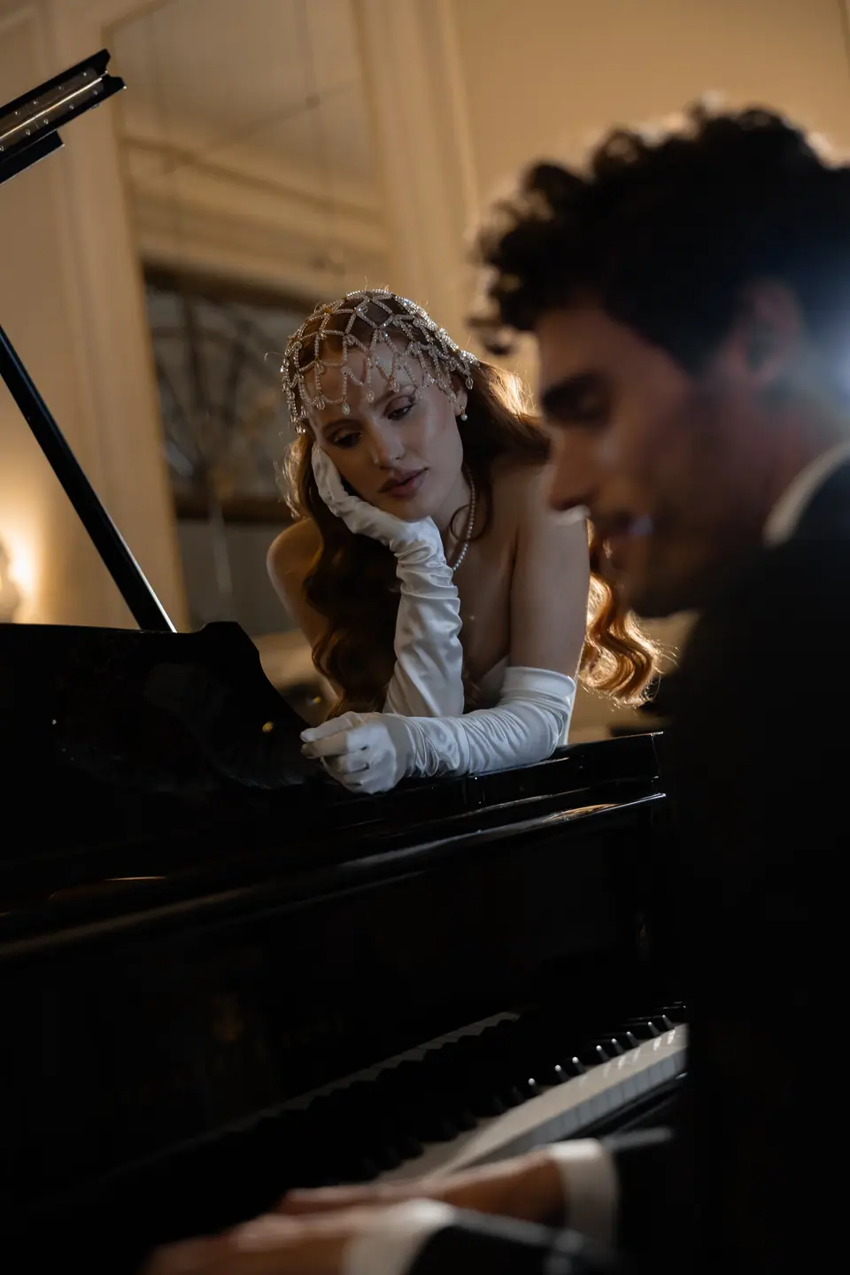 Roberta in white gloves and beaded headpiece leaning on the piano as Antoine plays