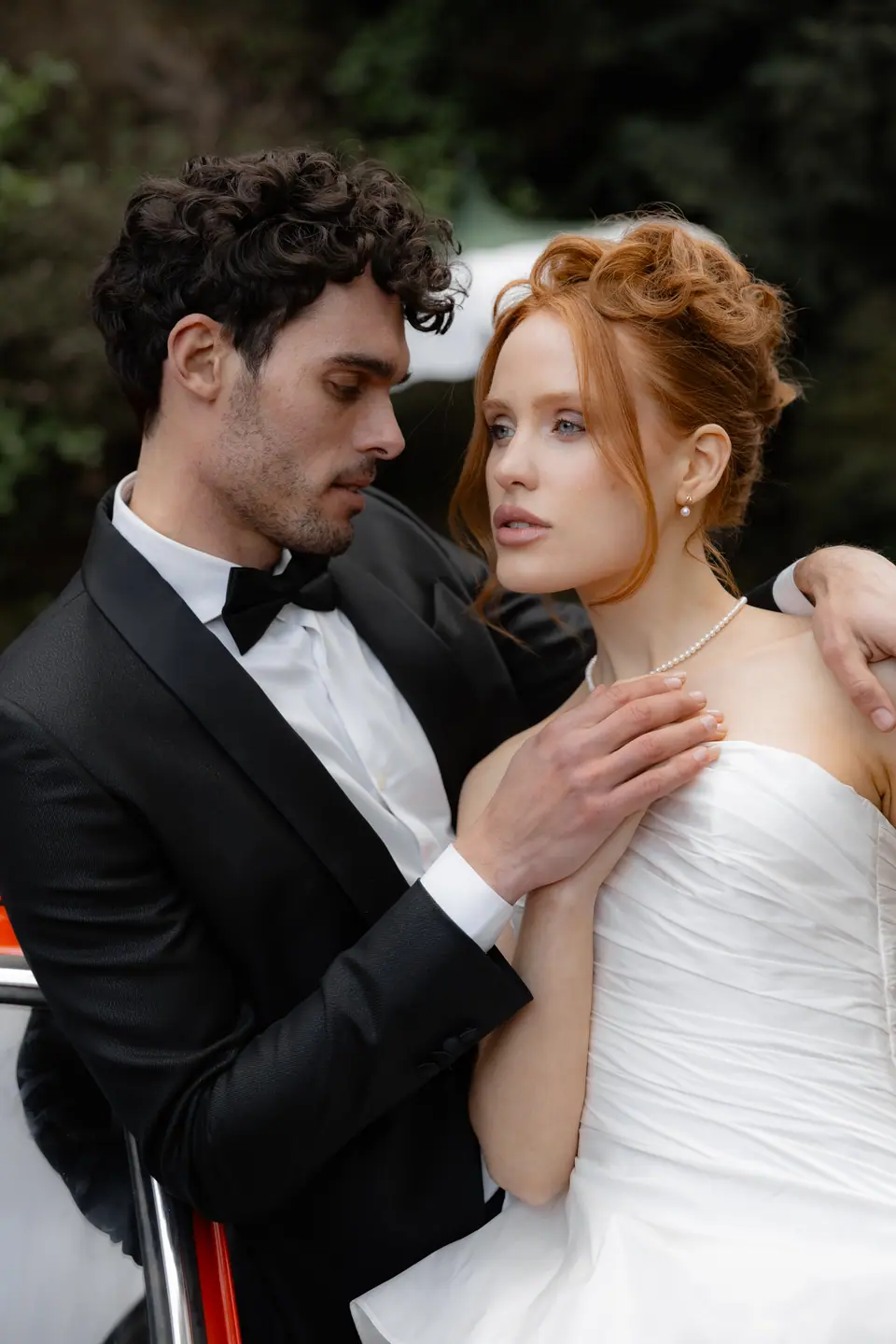 Antoine holding Roberta close beside a red car, a pearl necklace at her throat