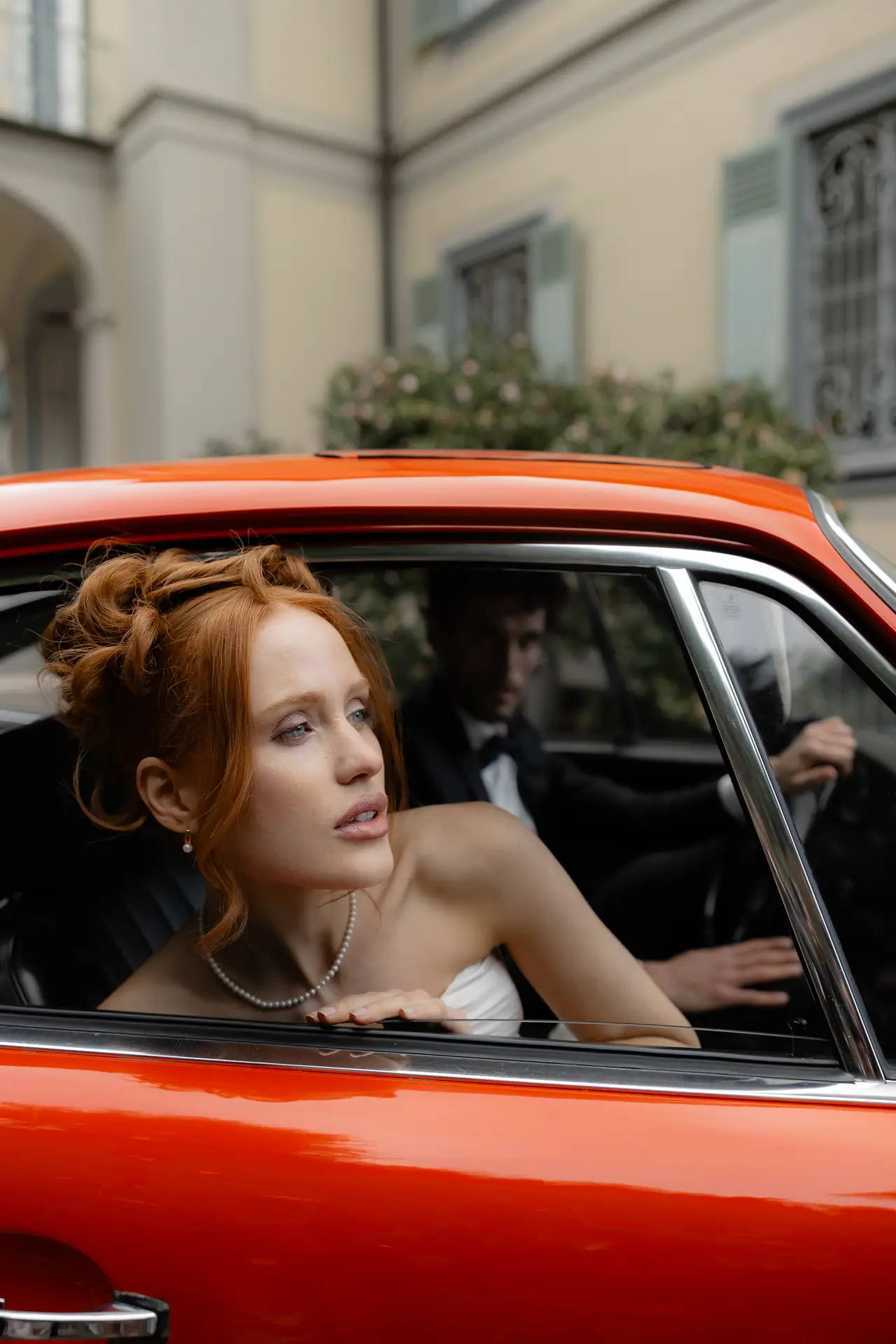 Roberta looking out of the window of a red vintage Porsche, Antoine at the wheel