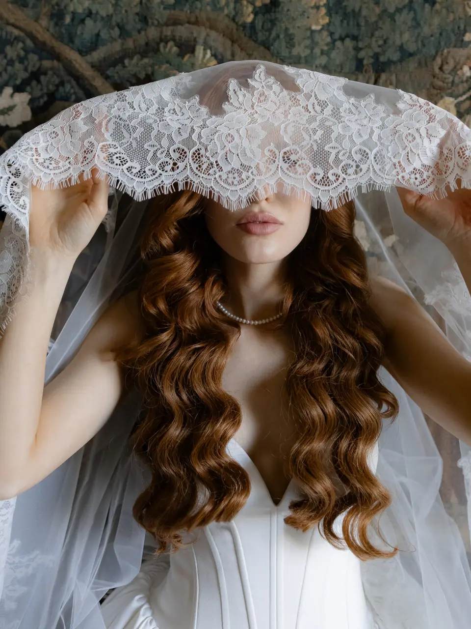 Roberta holding a lace veil over her eyes in front of a tapestry