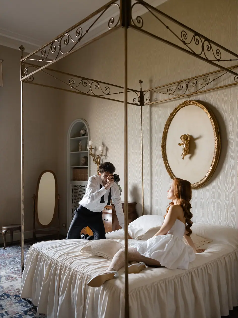 Antoine kneeling to photograph Roberta on the four-poster bed
