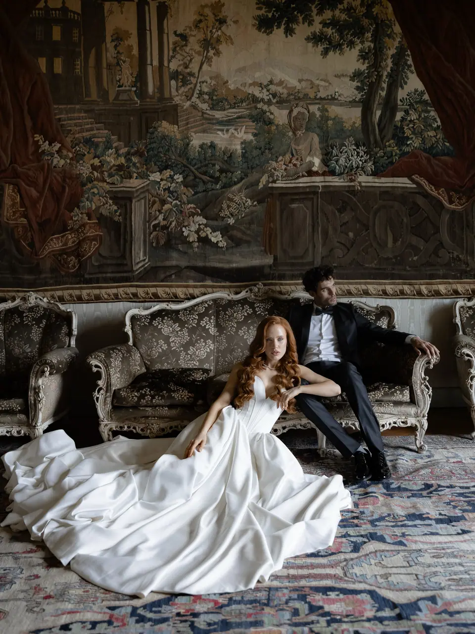 Roberta seated on a patterned rug in her full gown, Antoine on a sofa behind her